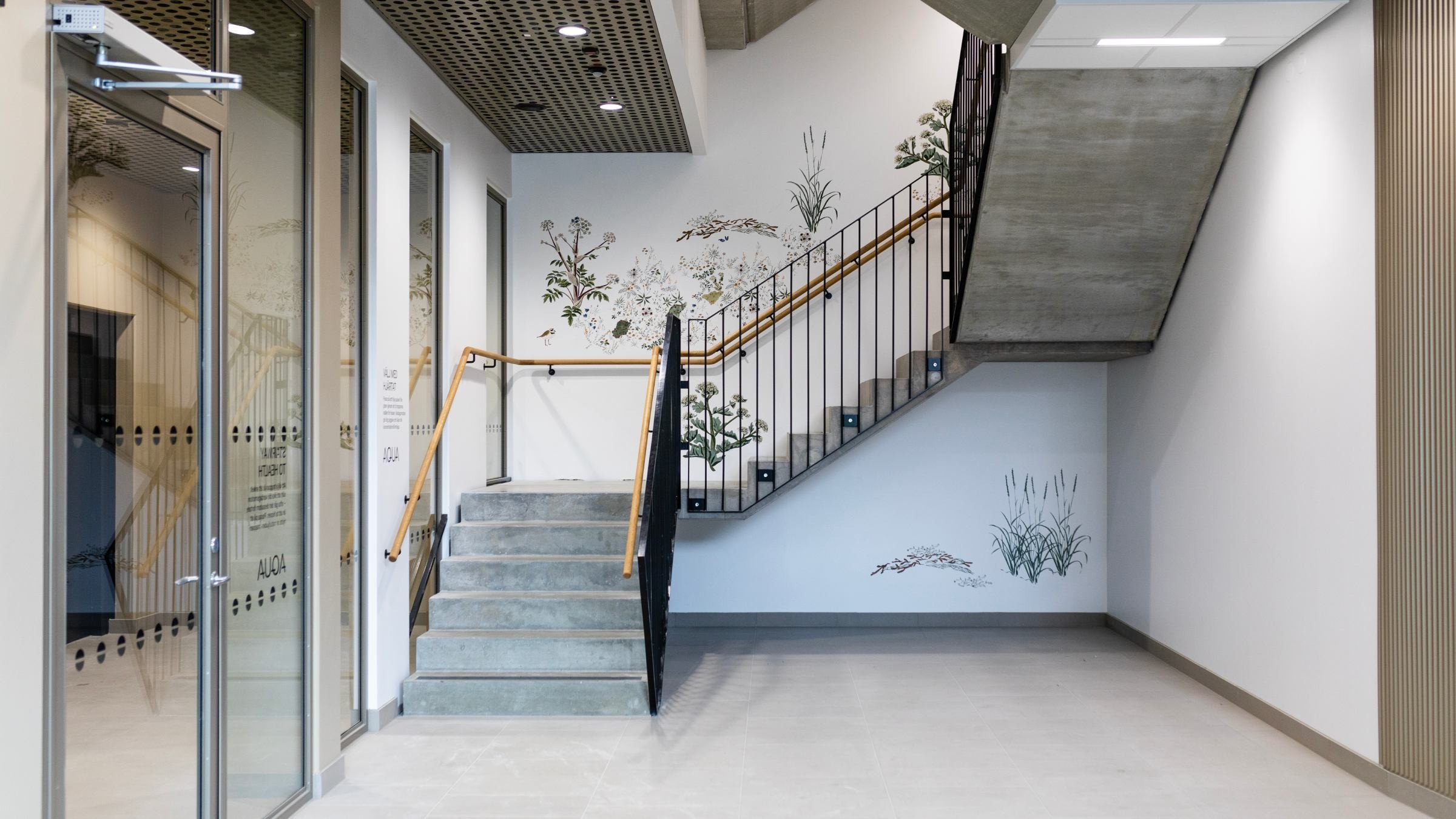 Modern inredning med betongtrappa, glasdörr och botanisk väggkonst i en ljus hall.