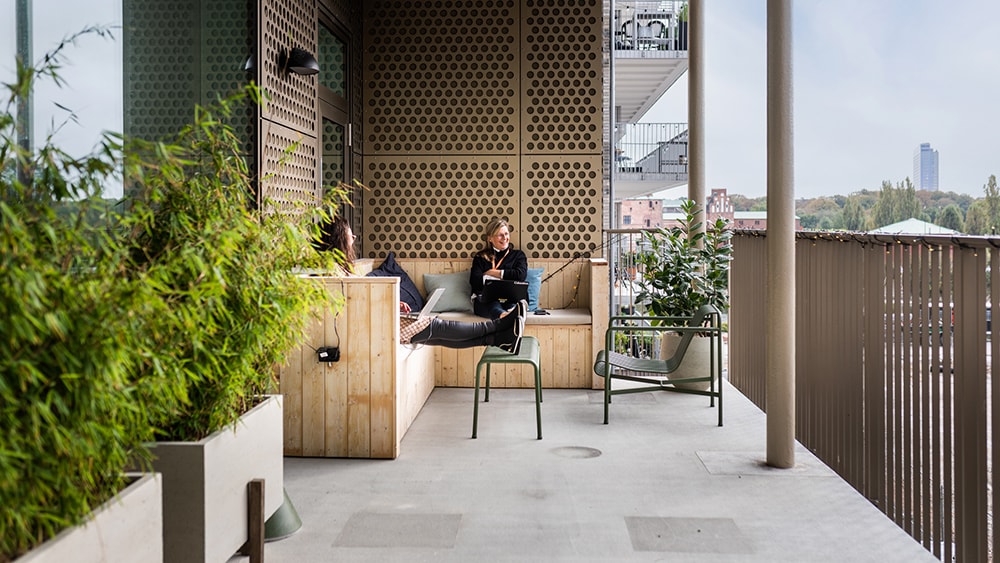 Two people relaxing on a modern balcony with potted plants and cityscape in the background.