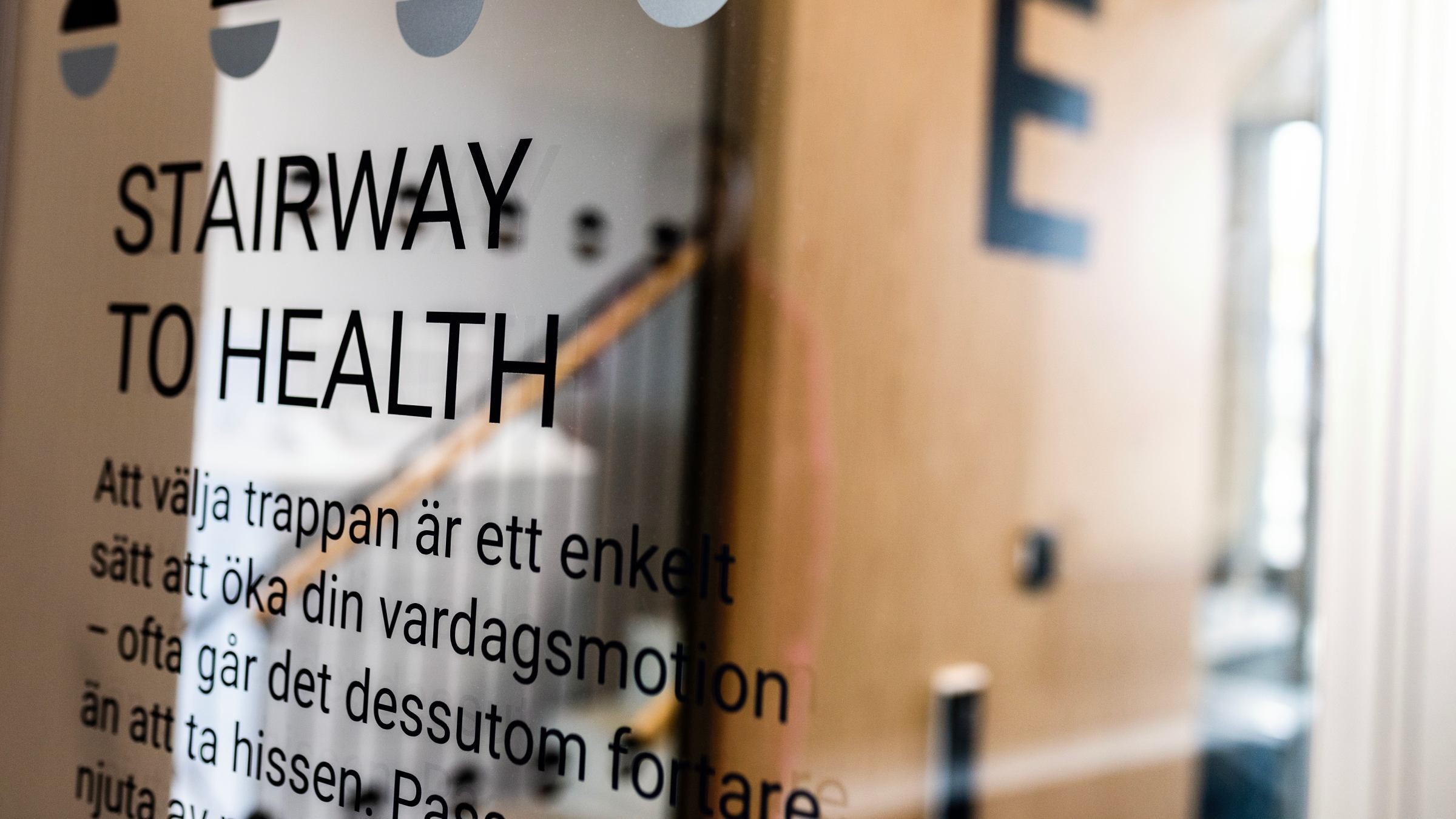 Glasdörr med skylten "TRAPPA TILL HÄLSA", främjar användning av trappor för daglig motion.
