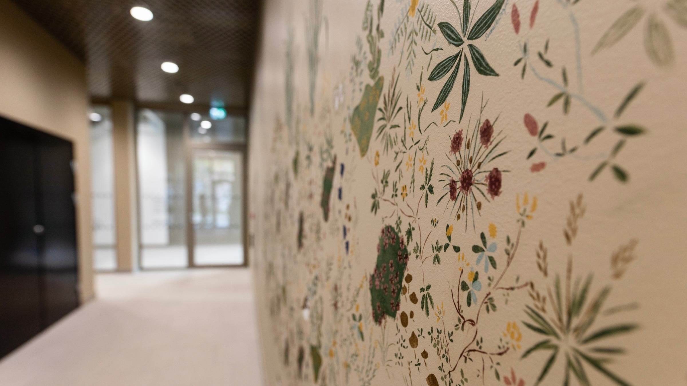 En hall har en botanisk väggmålning med olika färgglada blommor och blad på en beige vägg.