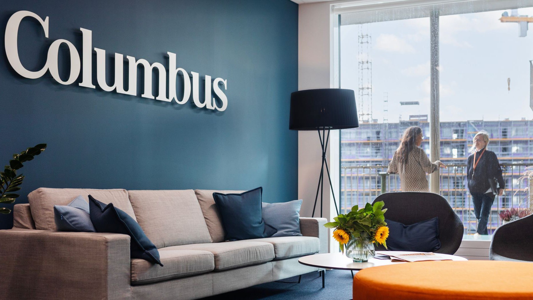 Modern kontorslounge med "Columbus"-skylt, en mysig sittgrupp och stort fönster med utsikt över staden.