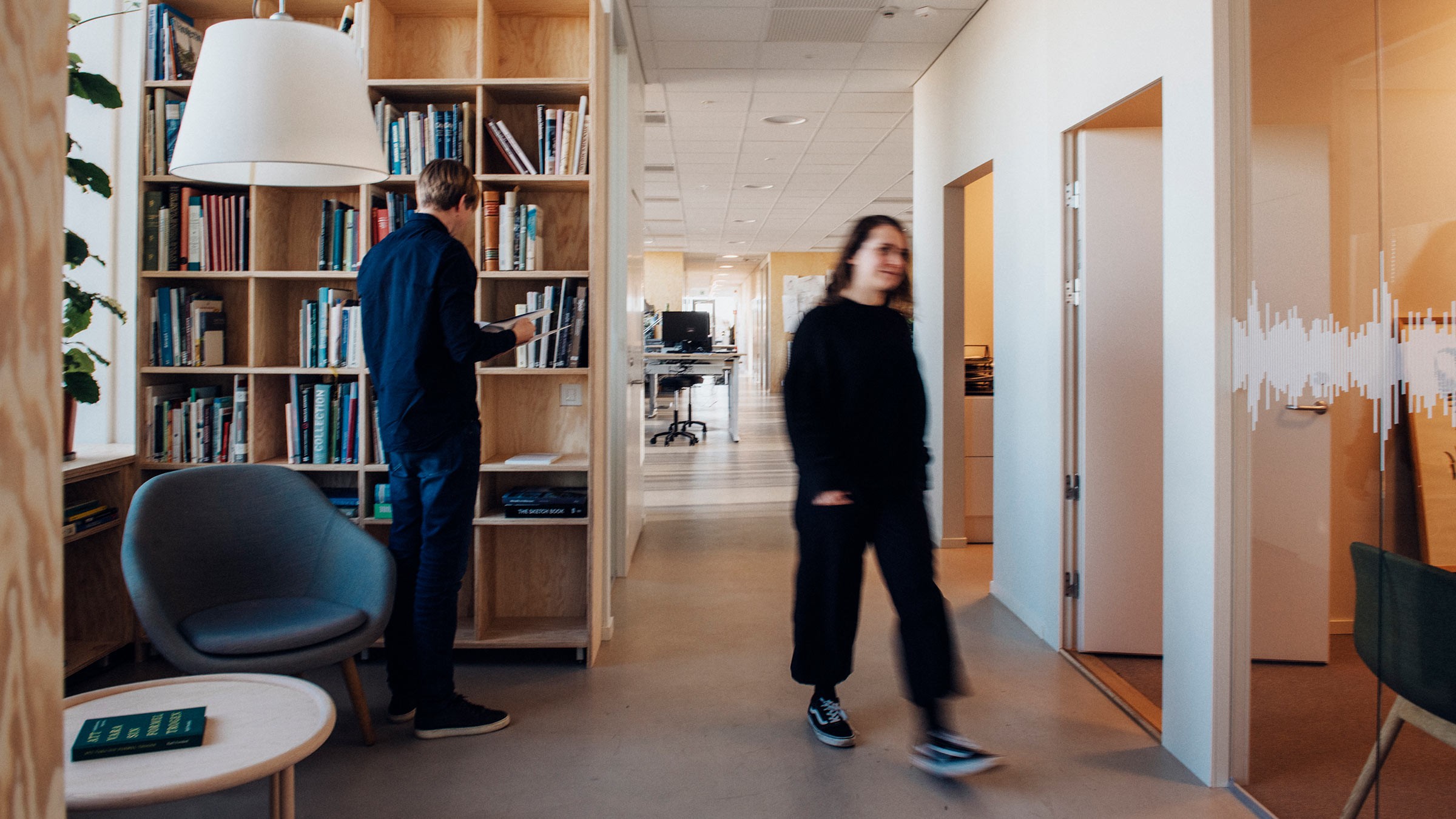 Modern Office Space with Bookshelves and Open Workspace Modern office interior with a person browsing books on a shelf, suggesting a creative workspace.