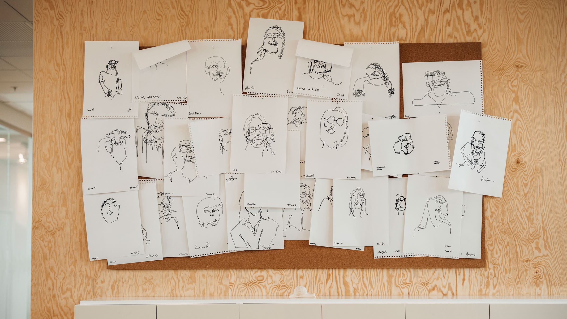 Unique Hand-Drawn Portraits Displayed on Cork Board A corkboard displaying various line art sketches of faces on paper, arranged in a casual collage.
