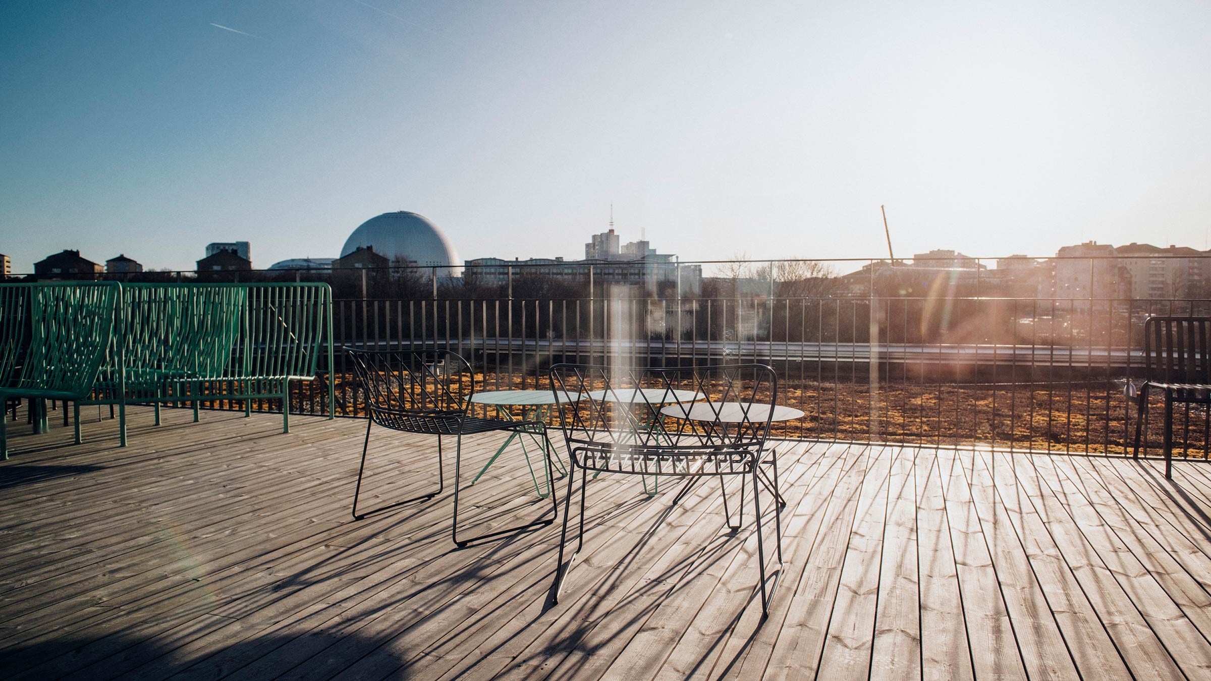 Sunny Rooftop Terrace with Cityscape View and Seating Area Sunlit rooftop patio with metal chairs and table overlooking a cityscape with a domed structure.