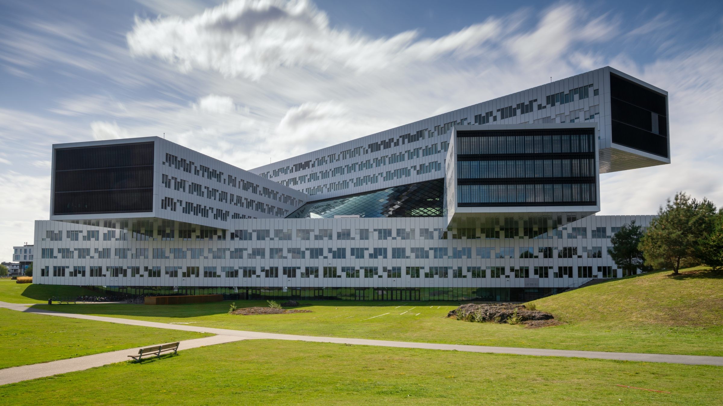 Modern kontorsbyggnad med unik lager-på-lager-design under en delvis molnig himmel.