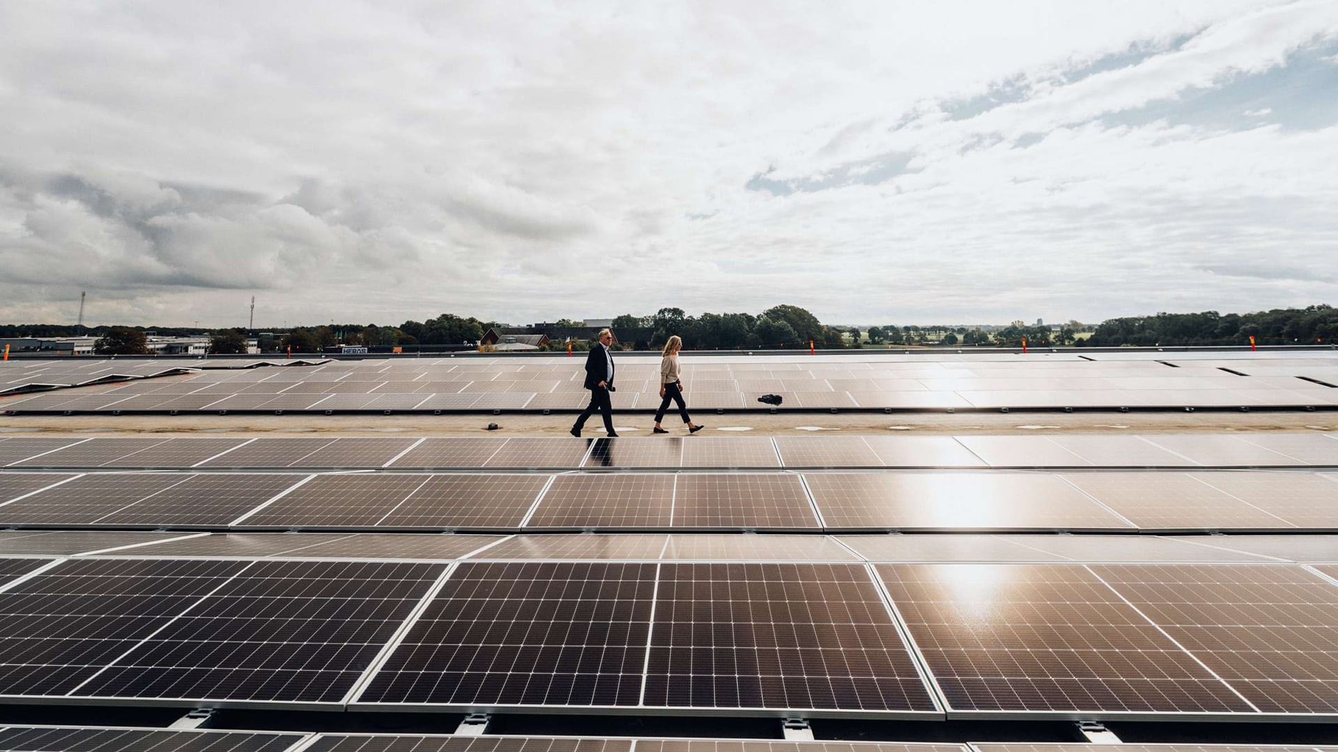 Människor som går på stor solpanelsinstallationsplats Två personer går över en stor solpanelsinstallation under en molnig himmel, vilket visar förnybar energi.