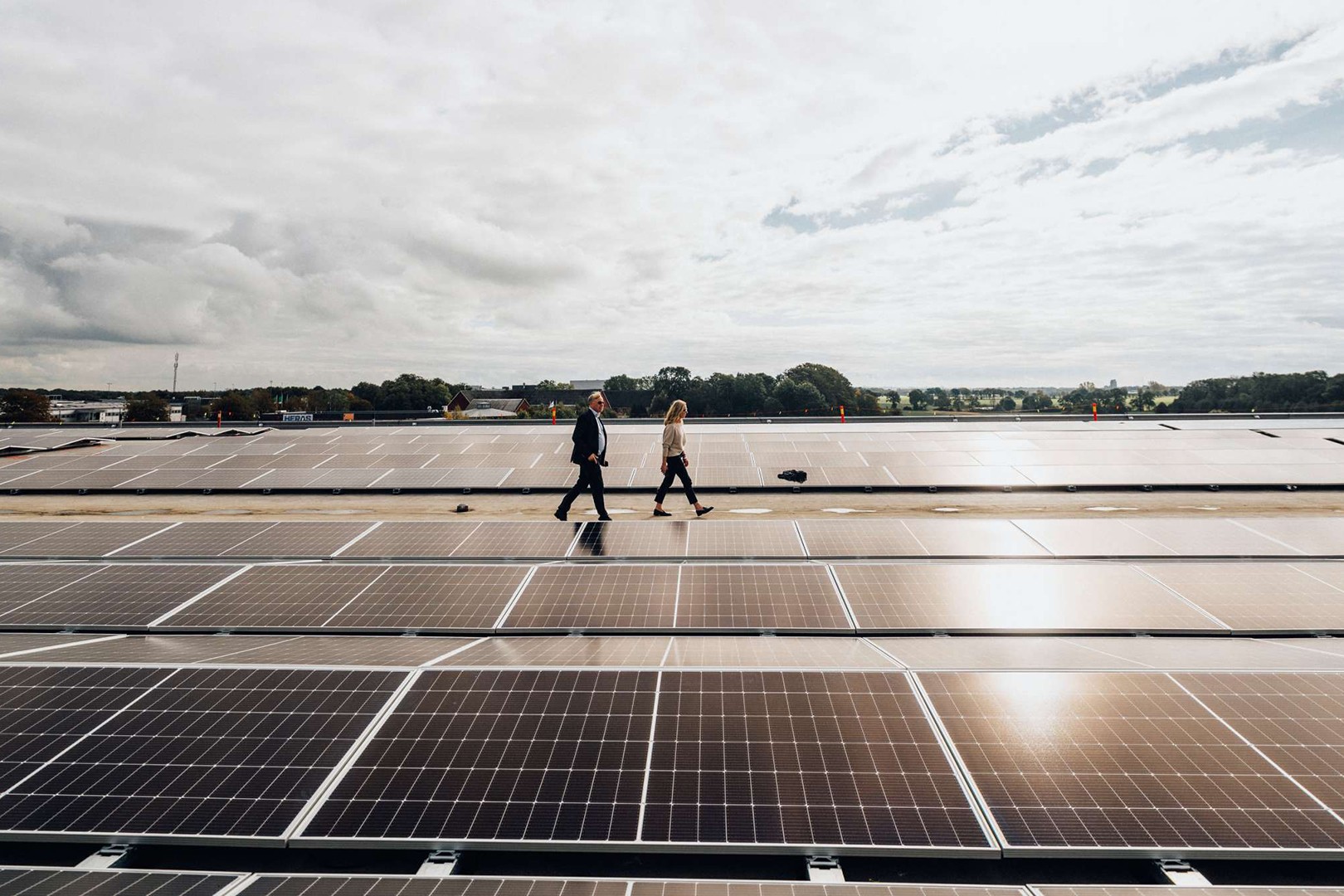 Gå på solpaneler: Hållbar energi i aktion Två personer går på en stor solpanelanläggning under en delvis molnig himmel, som visar förnybar energi.