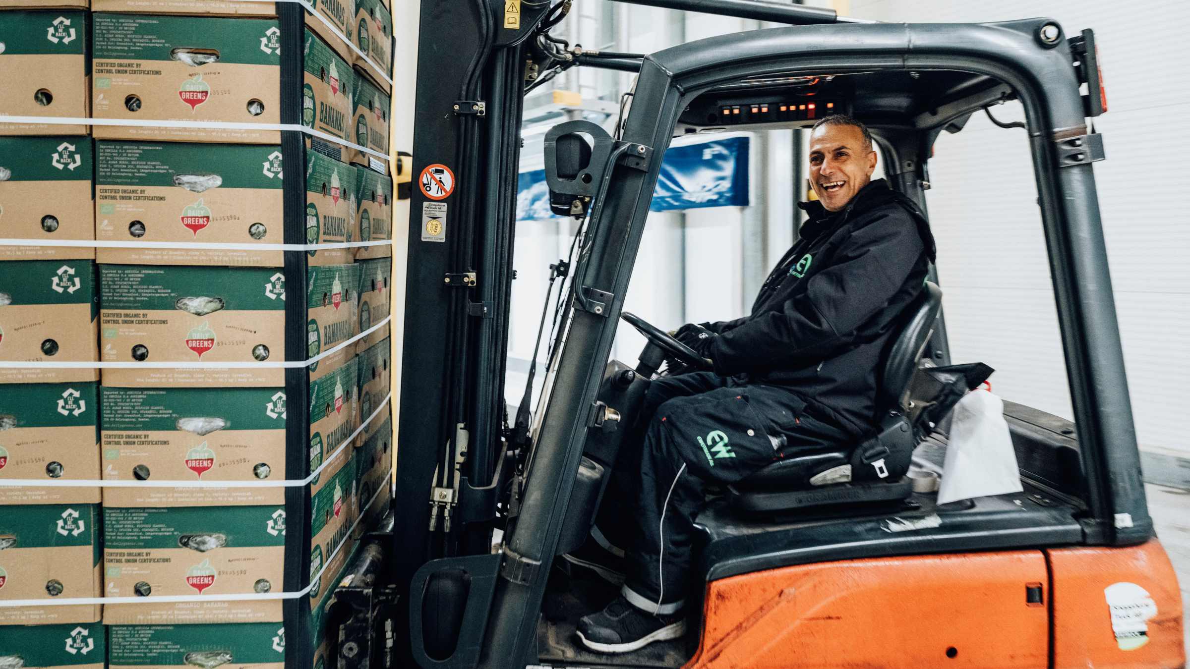 Gaffeltruckförare hanterar staplade kartonger säkert En truckförare transporterar staplade lådor i en lagerlokal.