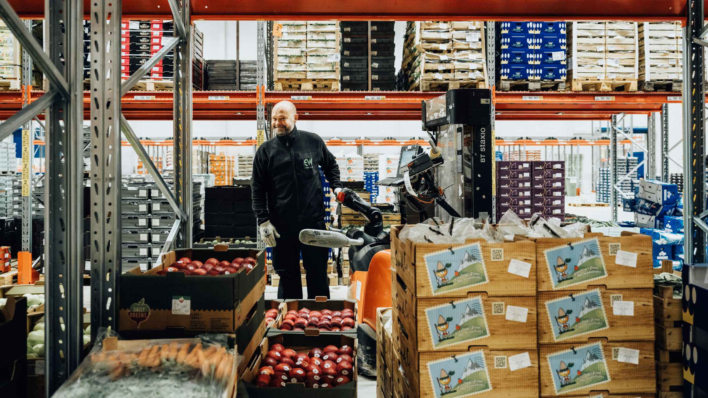 Lagerarbetare organiserar lådor med färska produkter Lagerarbetare organiserar lådor med färska produkter på hyllor, omgiven av olika frukter och grönsaker.