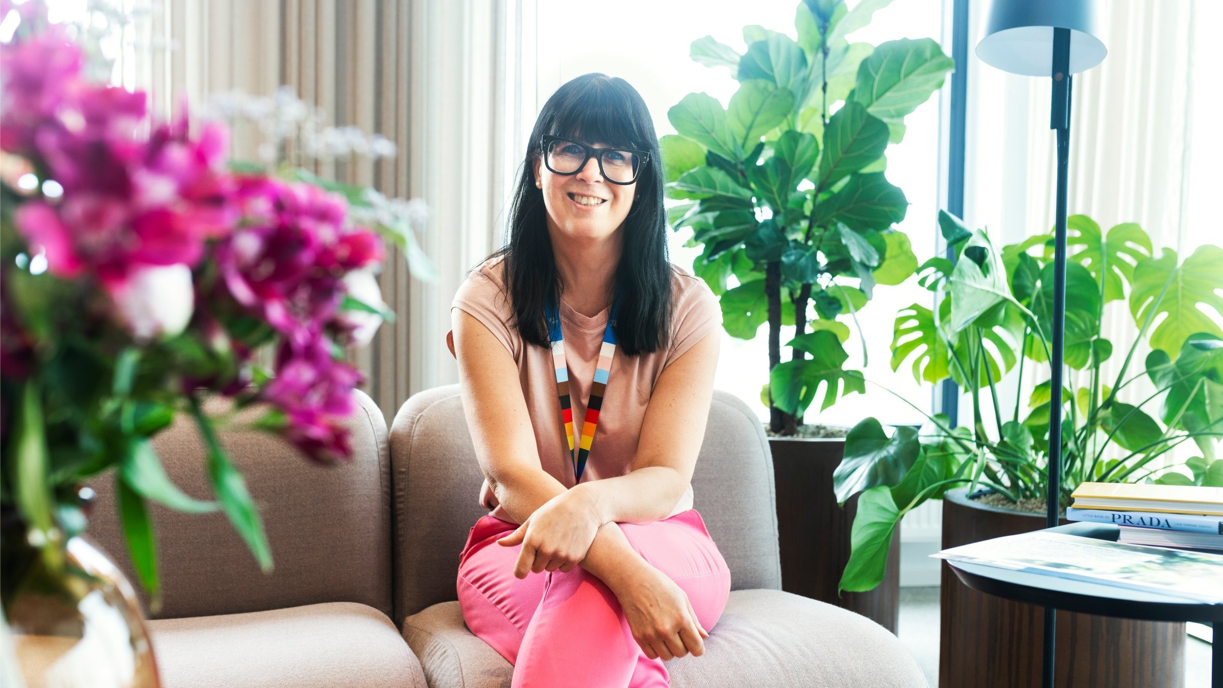 Stiligt modernt vardagsrum med livliga växter och dekorationer A person in colorful attire sits in a stylish, plant-filled living room, surrounded by vibrant decor.