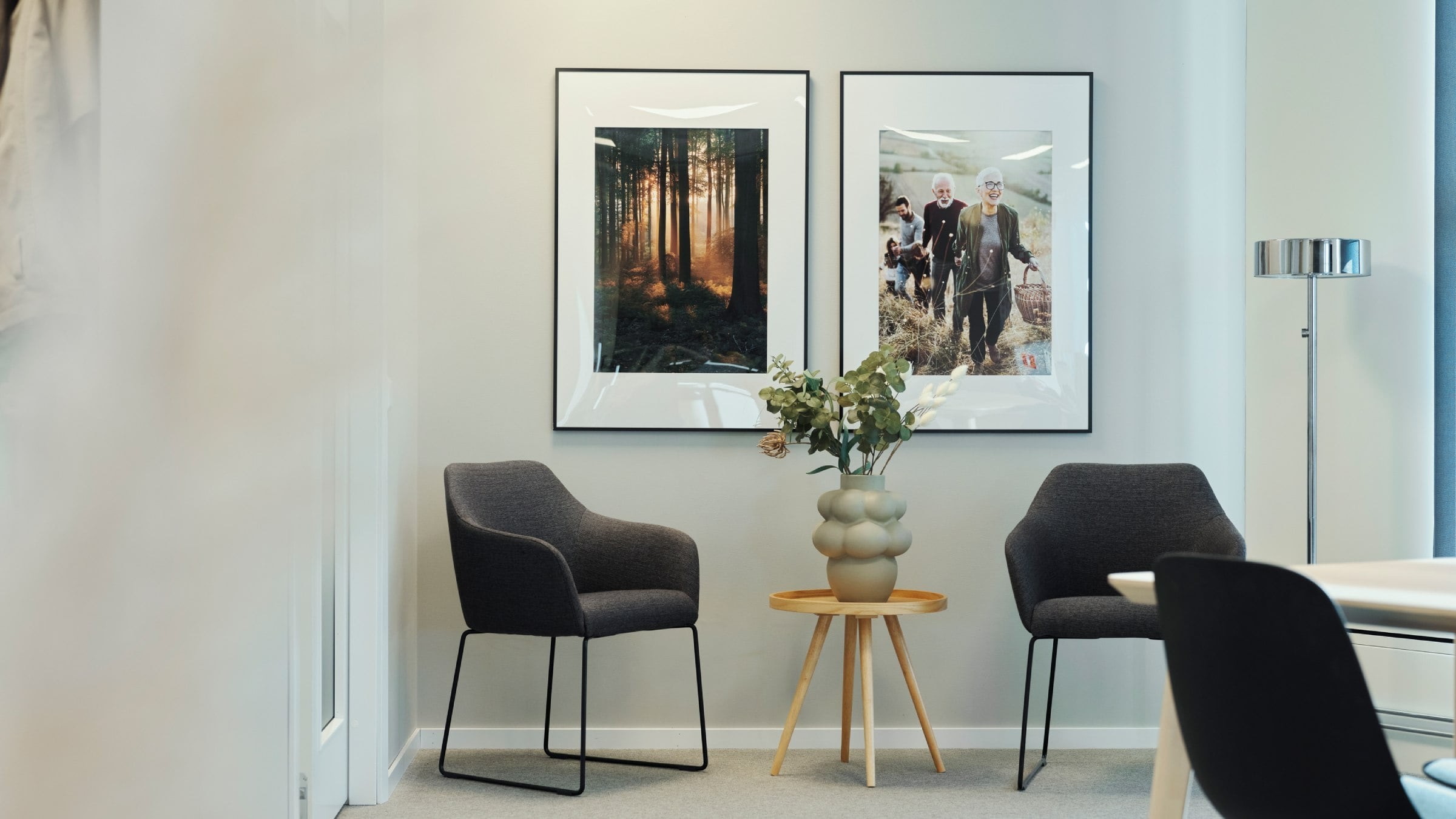 Modern kontorshörna med två fåtöljer, ett litet bord och inramade skogs- och gruppfoton.