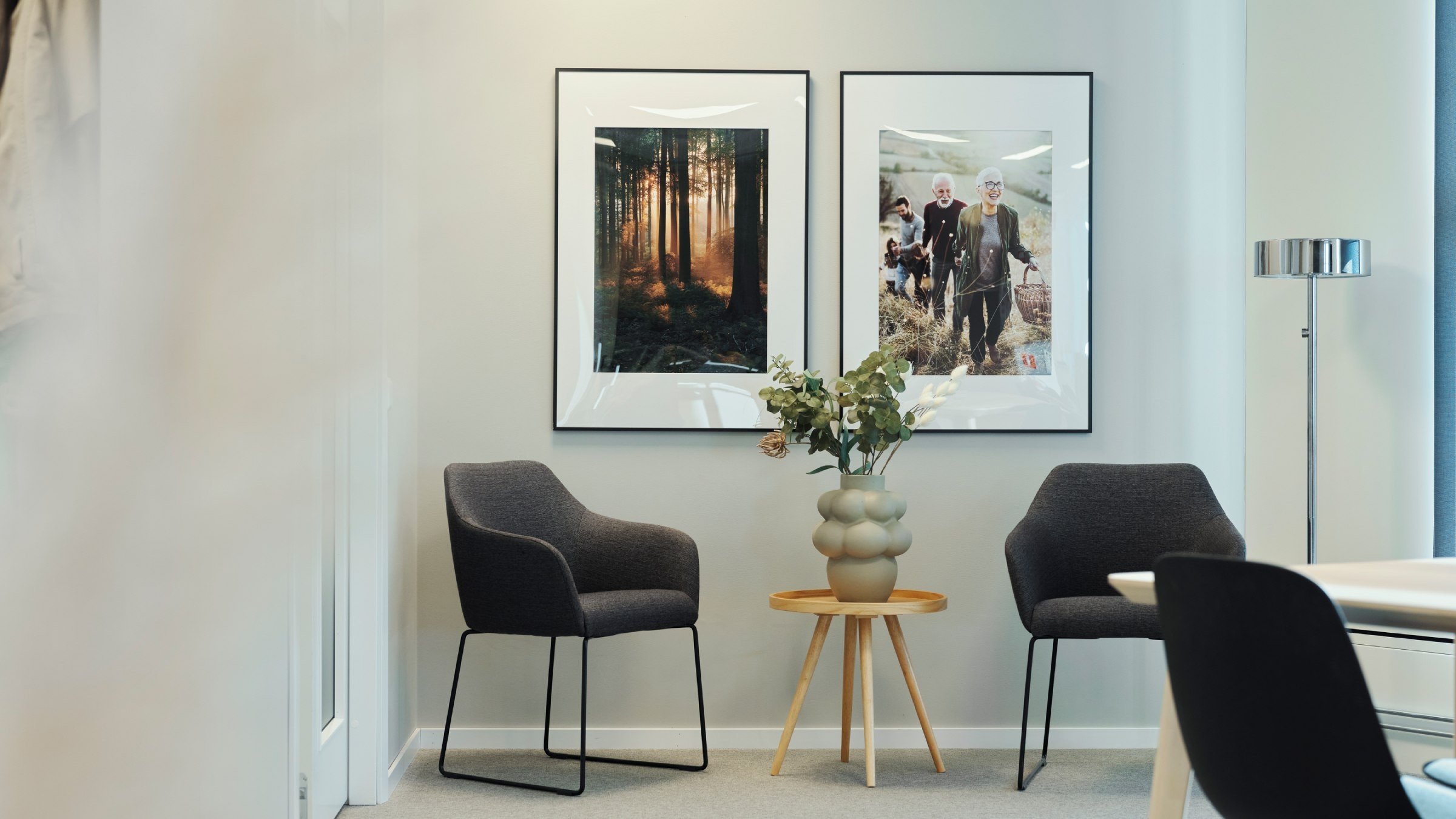 Modern kontorslounge med stilfull inredning och konsttryck Modern kontorshörna med två fåtöljer, ett litet bord och inramade skogs- och gruppfoton.