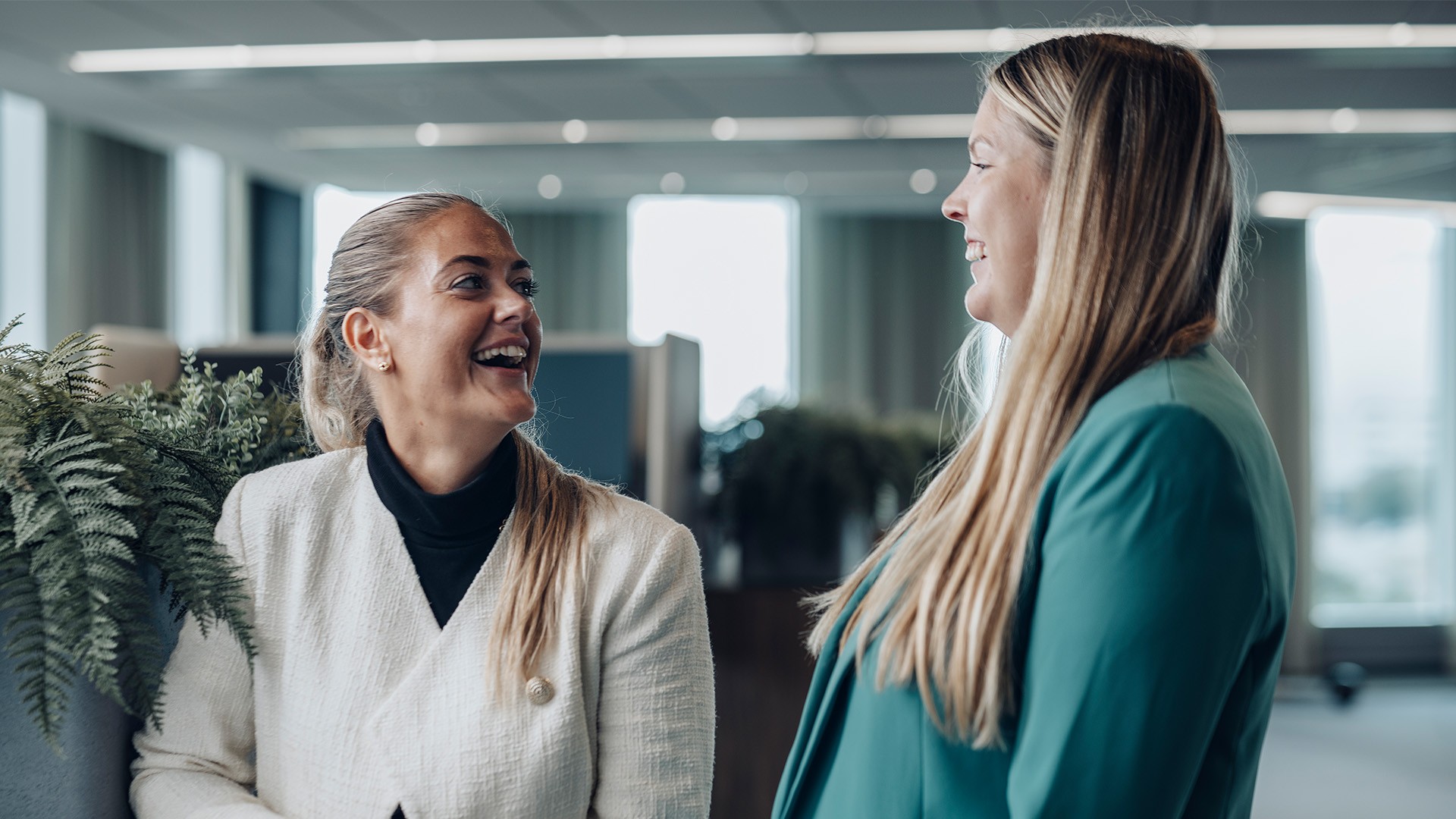 Professional Women Networking in Modern Office Environment Two women in professional attire engaged in conversation in a modern office setting.