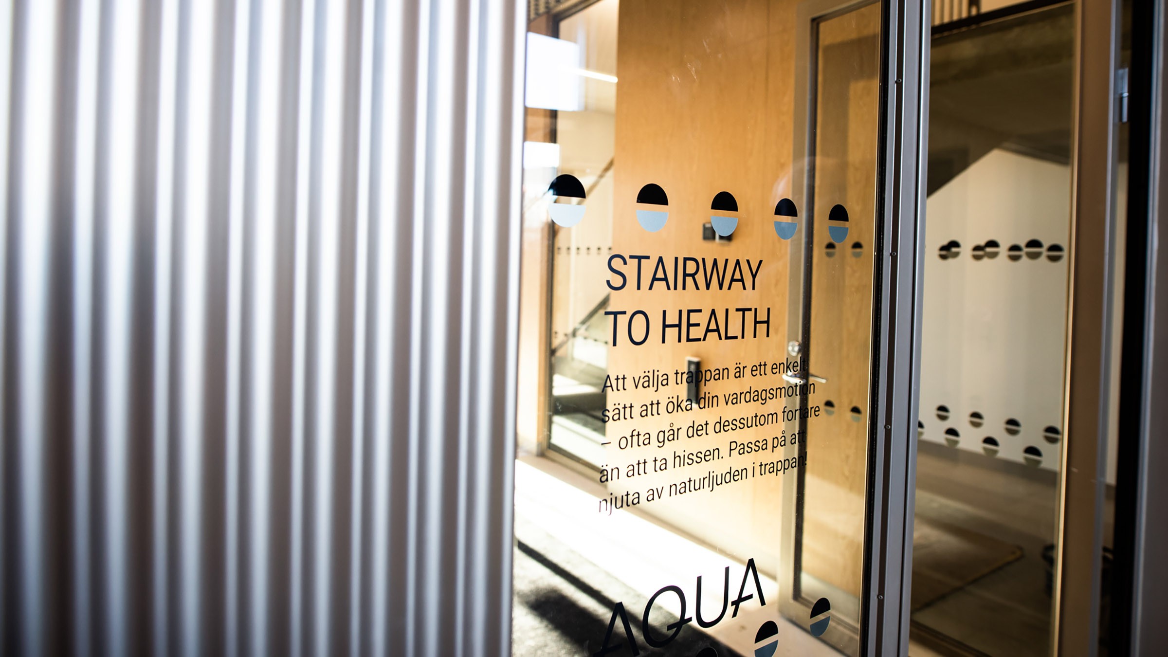 Glasdörr med skylt "Stairway to Health" som leder till en modern inomhustrappa.