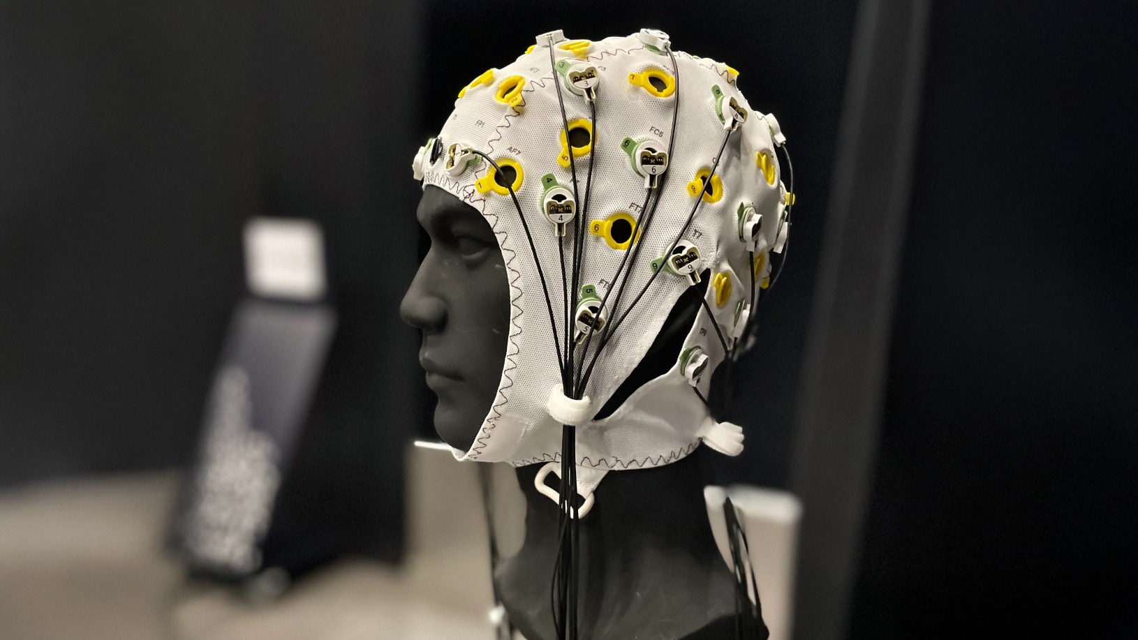 En vit EEG-mössa med flera elektroder och färgglada anslutningar på en mörk bakgrund.