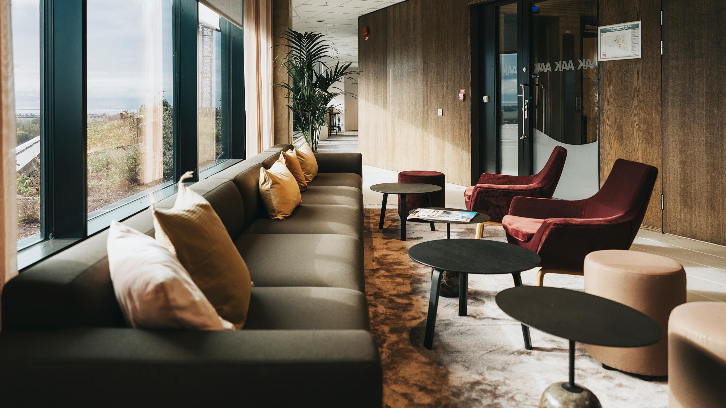 Modern kontorslounge med mysiga sittplatser och naturligt ljus Modern loungeområde med en lång soffa, mysiga fåtöljer och stilren inredning nära stora fönster.