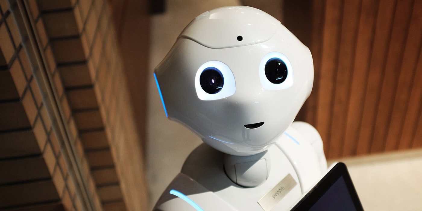 Vänlig humanoid robot med upplysta ögon på kontor. En vänlig humanoid robot med lysande ögon står inomhus och håller en surfplatta.