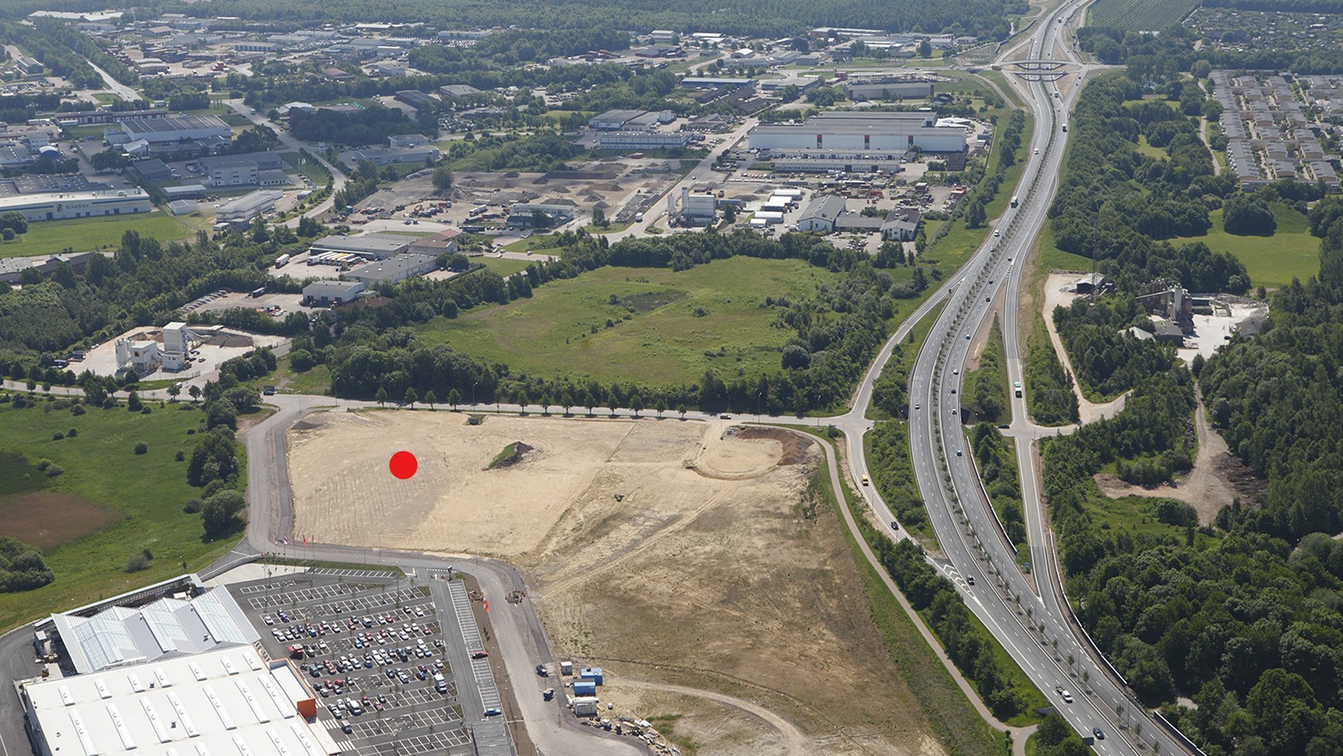 Aerial View of Industrial Area Near Highway and Green Spaces Aerial view of a commercial area with a red dot marking a construction site near a highway.