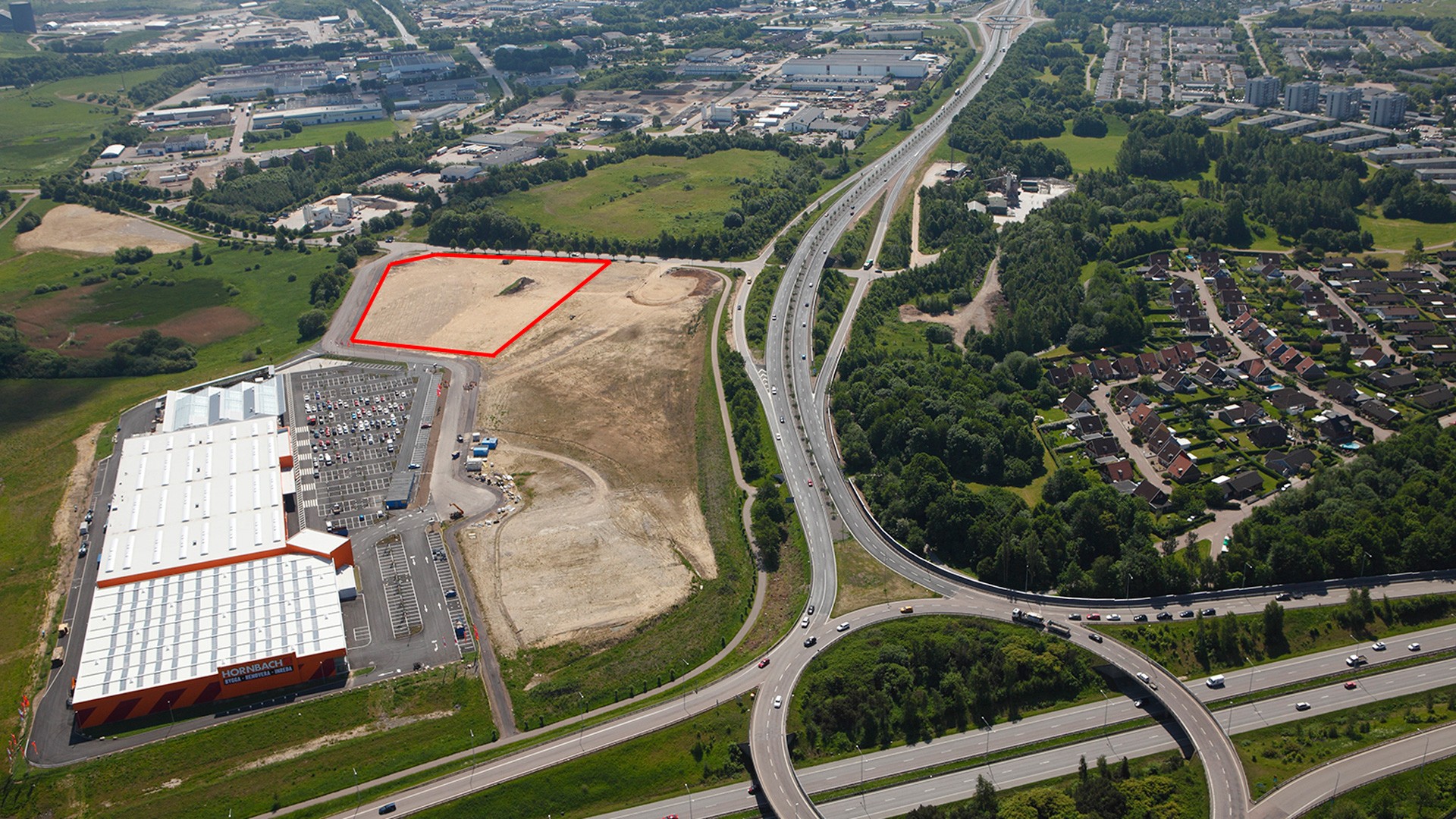 Aerial View of Industrial Site with Red Boundary Markings Aerial view of a commercial area with a marked plot near highways and a residential neighborhood.