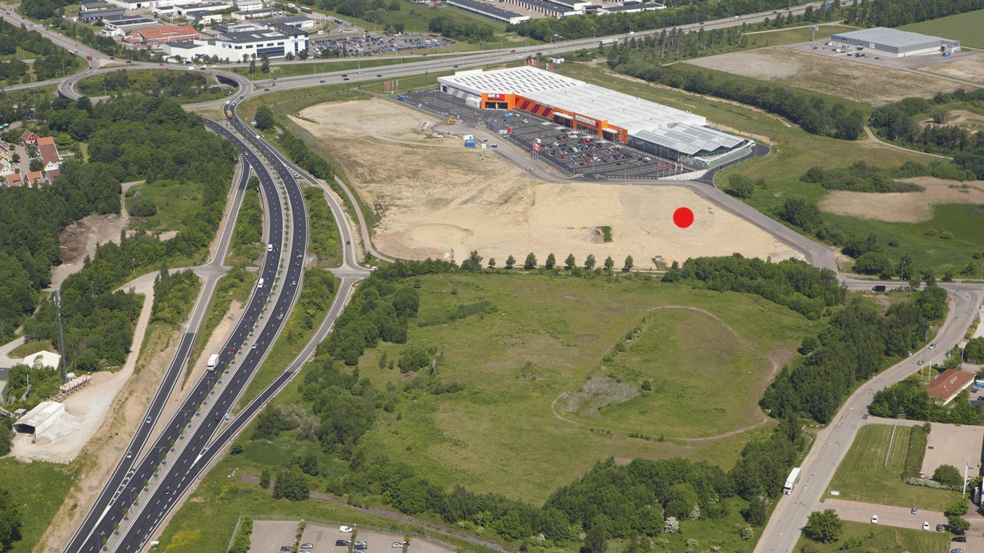 Aerial view of a highway adjacent to a large retail store with a parking lot and surrounding greenery.