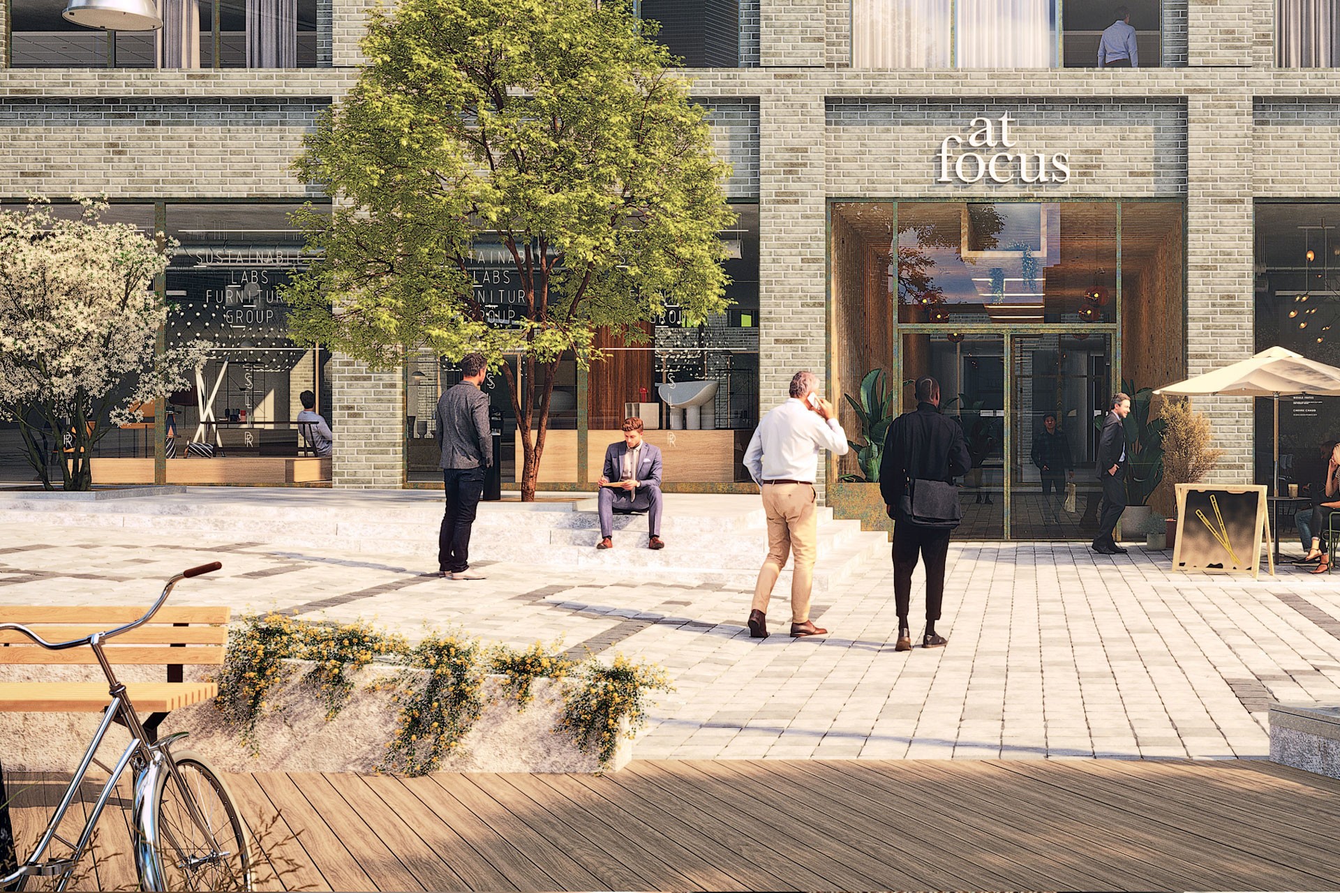Modern stadsplats med människor som samtalar utanför en byggnad märkt "at focus," med grönska.