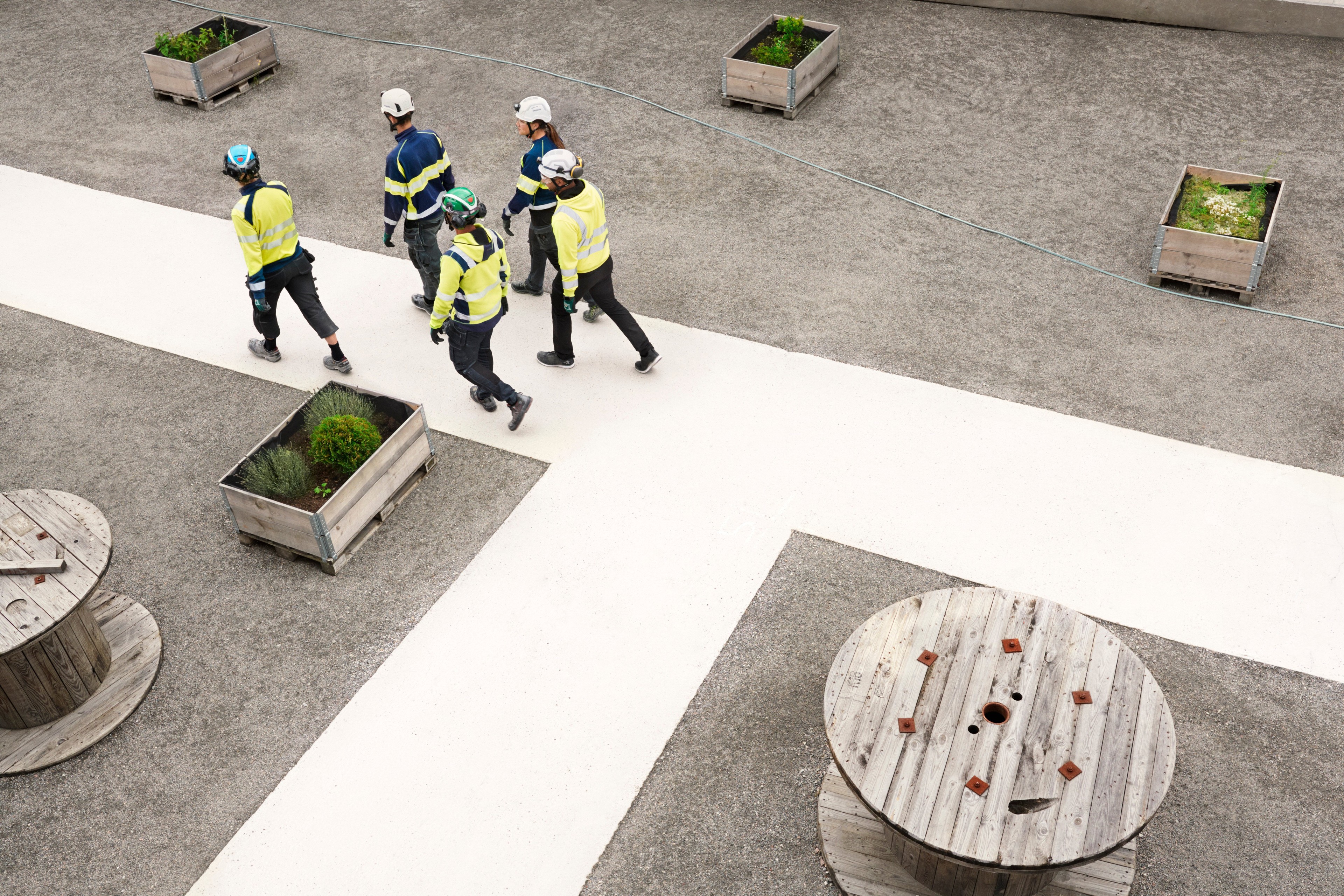 Grupp av arbetare i säkerhetsutrustning som går på en betongstig med träkrukor och spolar i närheten.