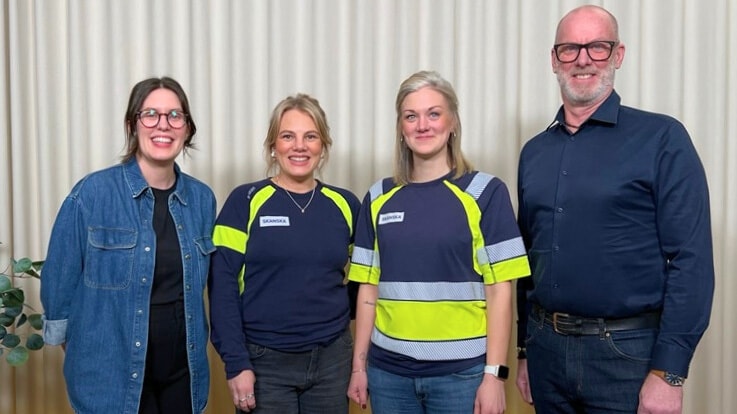 Four people stand in front of a curtain, two wearing reflective uniforms, in a casual group photo.