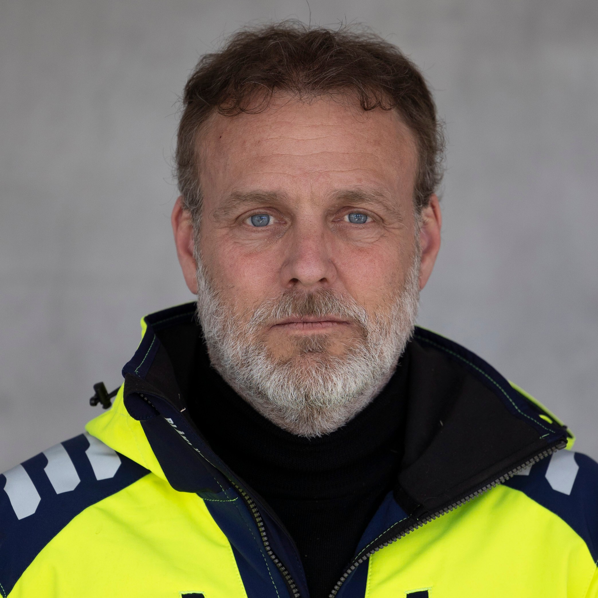 Anders Widell En person med en högsynlig jacka står mot en grå bakgrund.