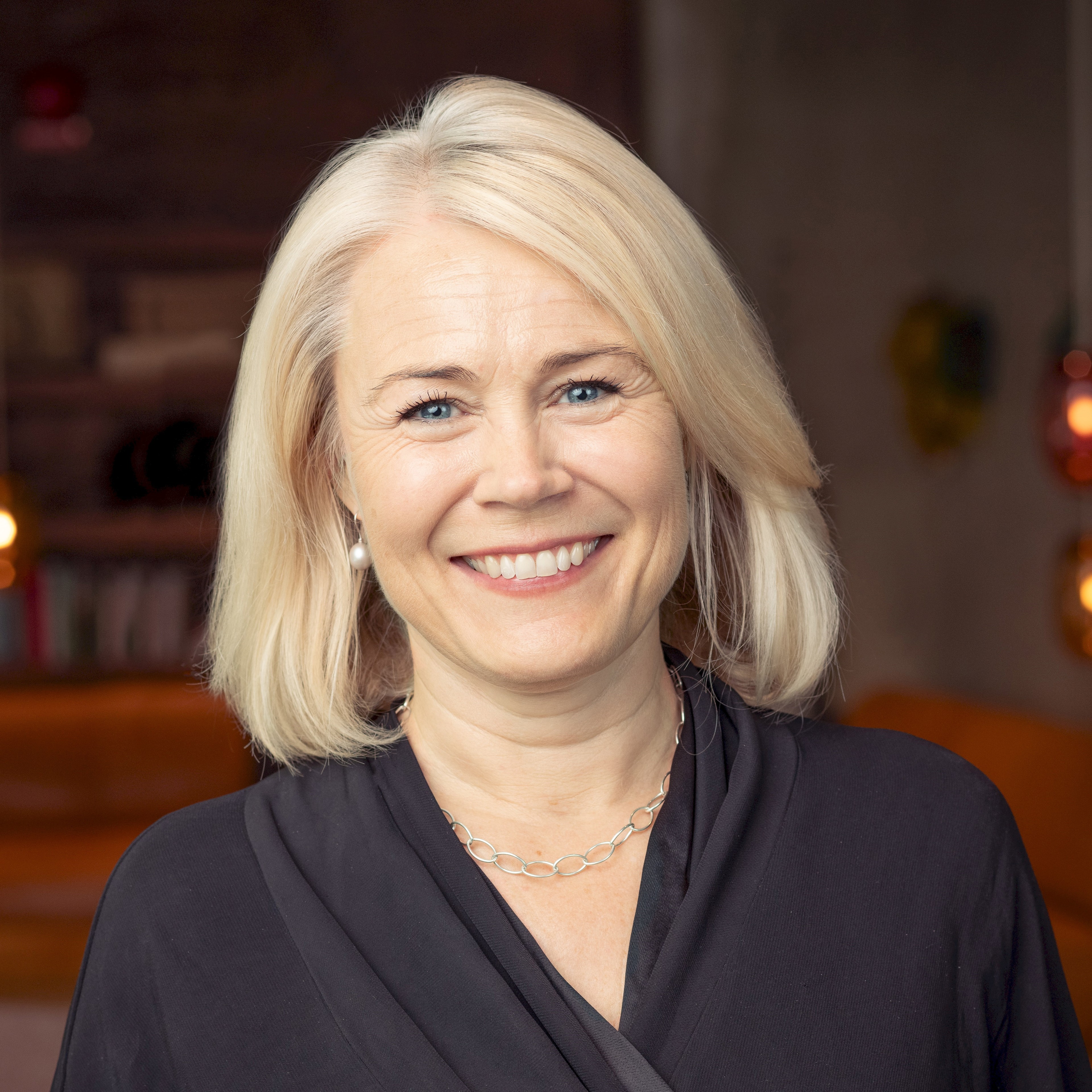 Britta Cesar Munck Person med blont hår som bär en svart topp i en mysig inomhusmiljö.