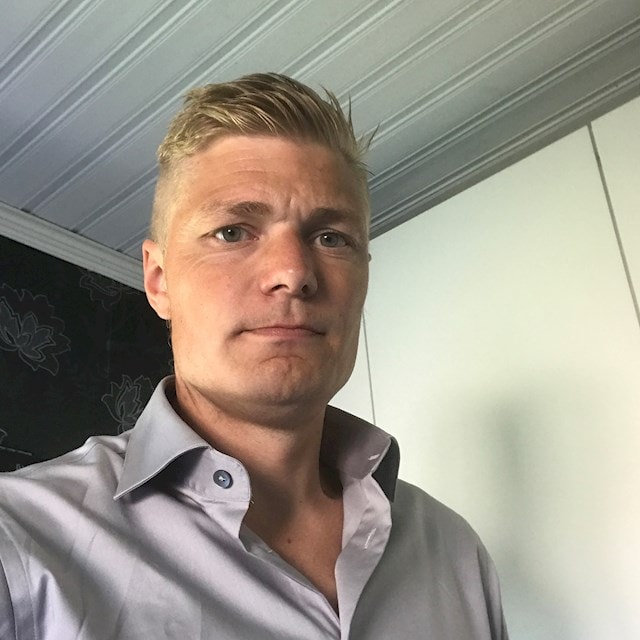 Christian Jakobsson A person wearing a light gray shirt with buttons with a modern interior as the background.