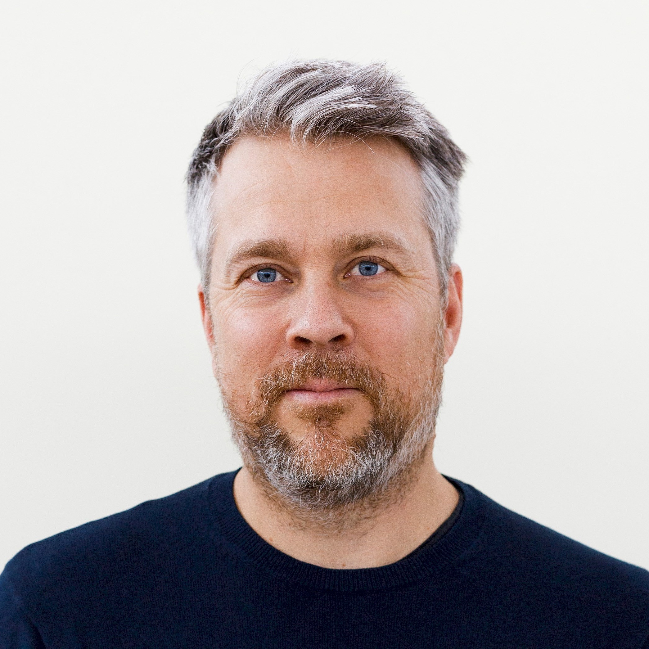 Daniel Beyer En man med grått hår och skägg som har på sig en mörk tröja står mot en enkel vit bakgrund.