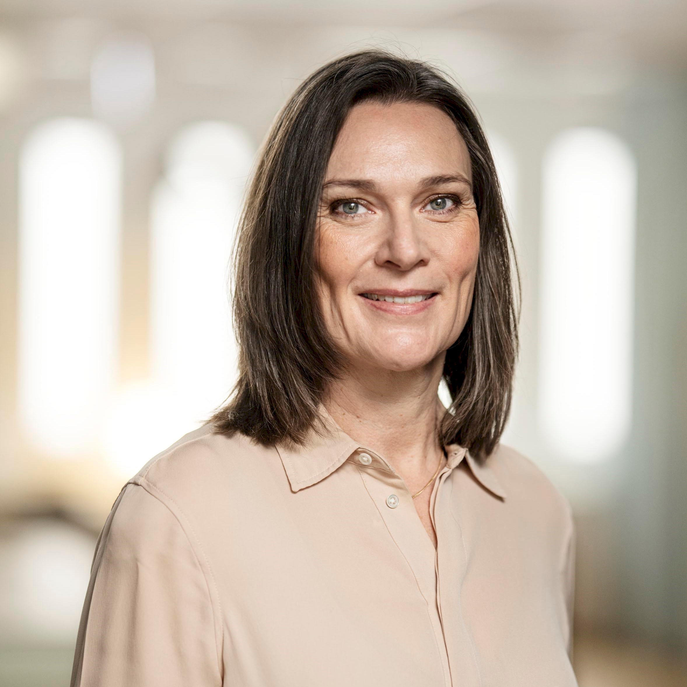 Elisabeth Hoffsten Kvinna i beige blus med axlelångt brunt hår.