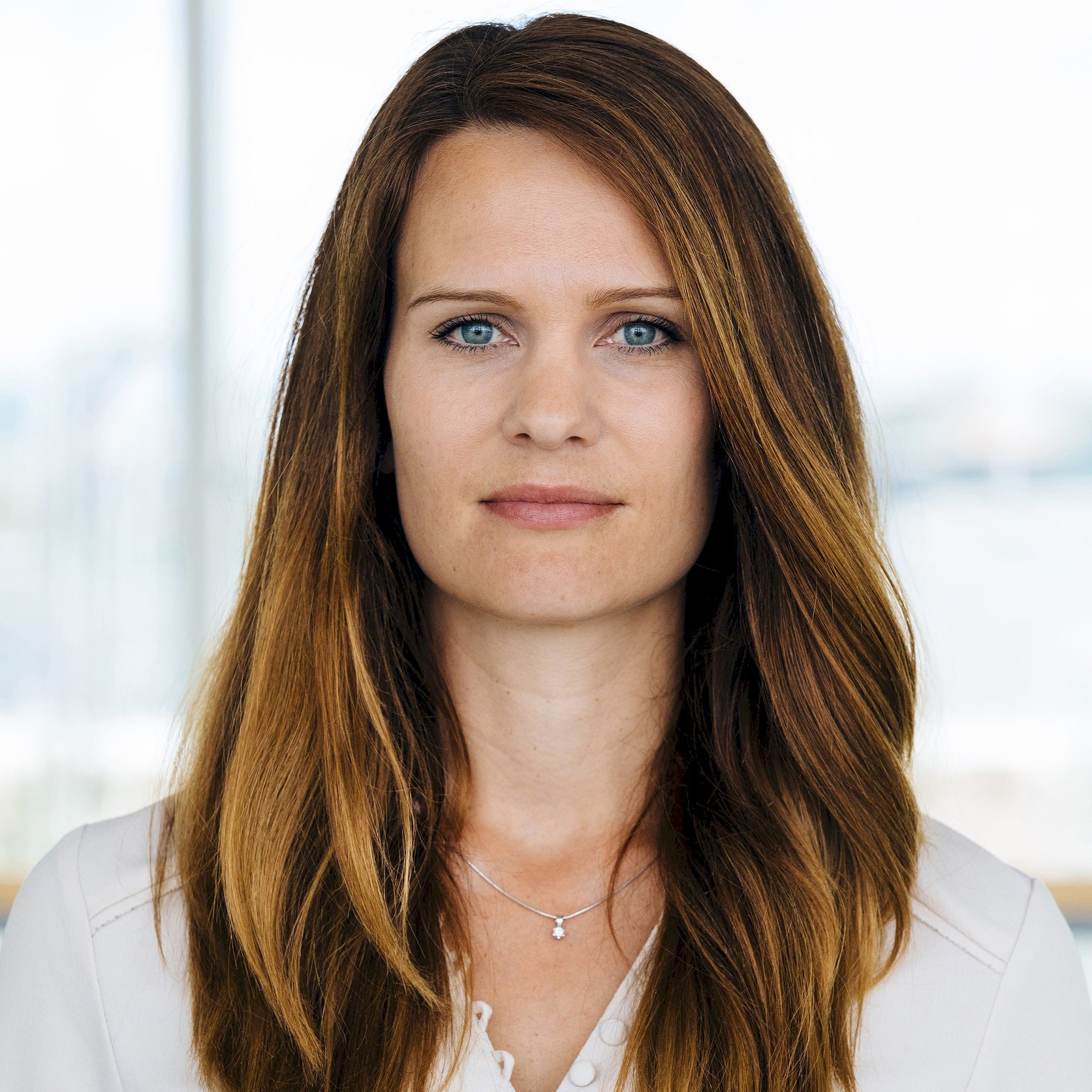 Person med långt brunt hår som bär en vit blus och ett silverhalsband.