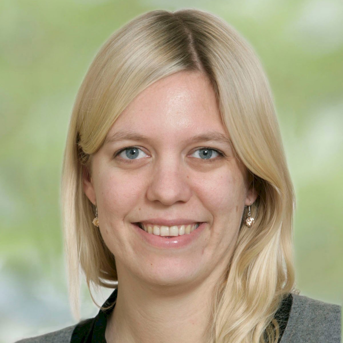 Jenny Ivarsson En person med långt blont hår och en svart topp, placerad mot en suddig grön bakgrund.