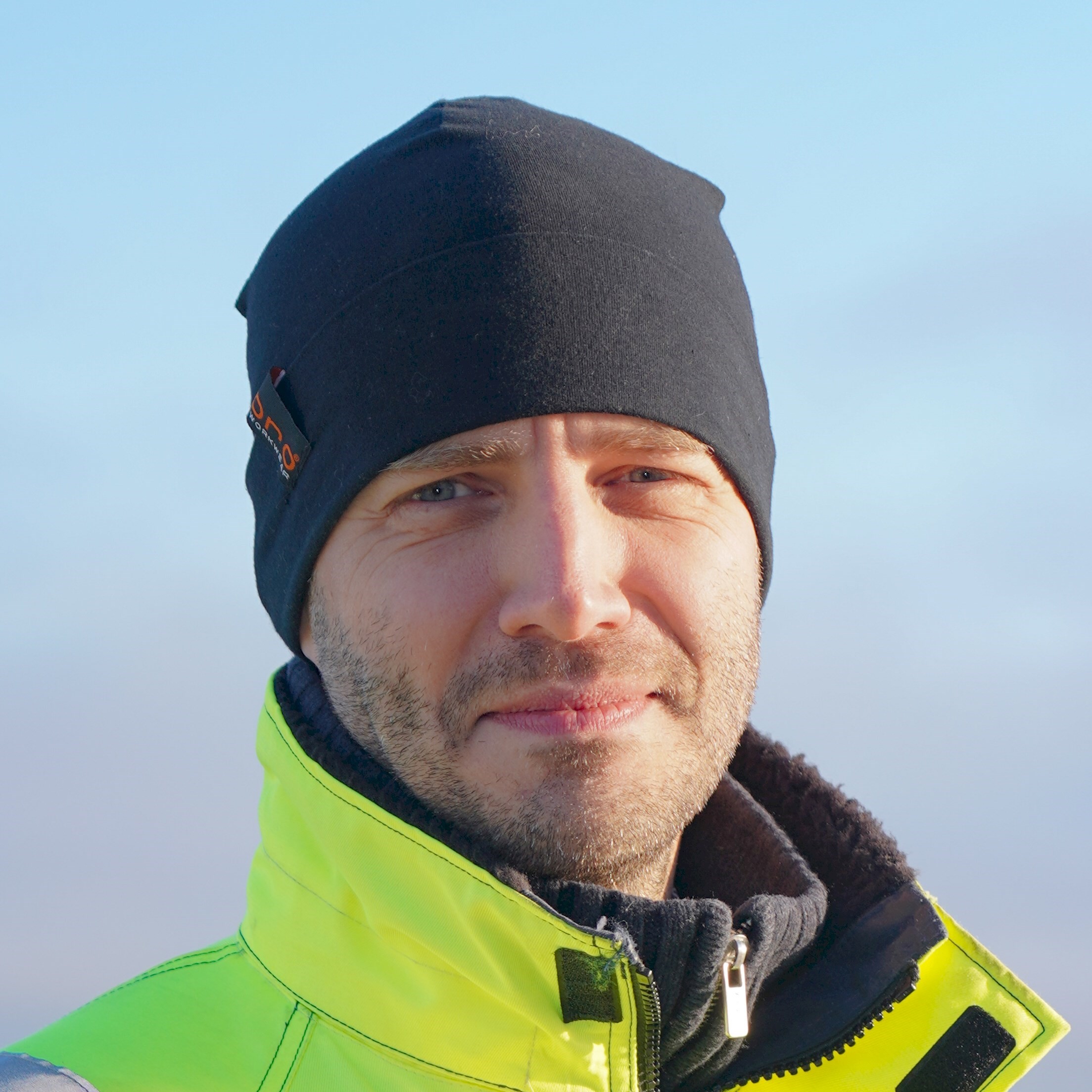 Johan Svensson Person som bär en svart hatt och neon gul jacka med dragkedja, står utomhus.