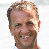 Klas Heed En man med kort, ljusbrunt hår står utomhus med en sjö i bakgrunden.