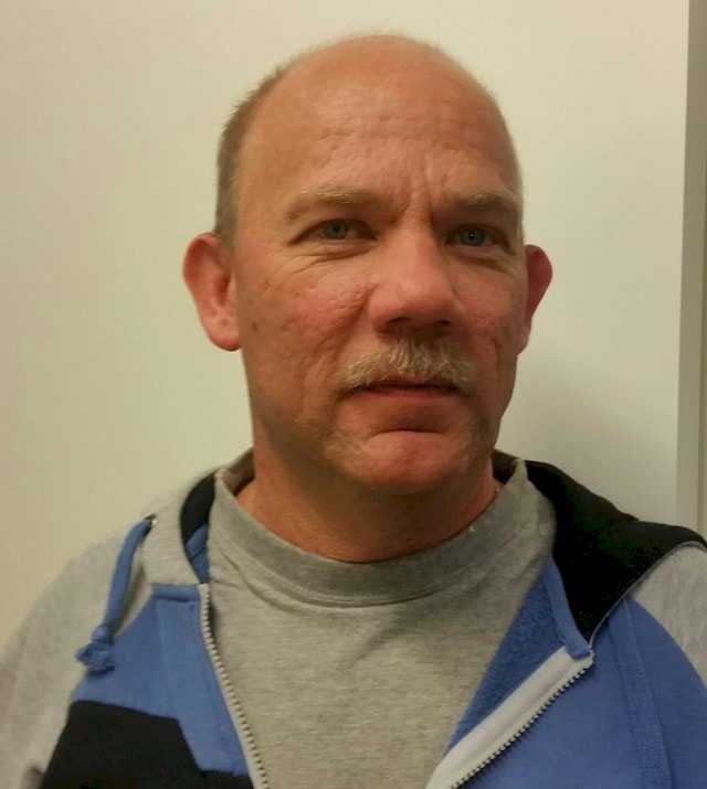 Lars Sandkvist Man in a gray and blue zip-up hoodie stands against a white wall.