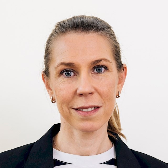 Lisa Kroon Person med brunt hår uppsatt, klädd i svart kavaj och randig skjorta.
