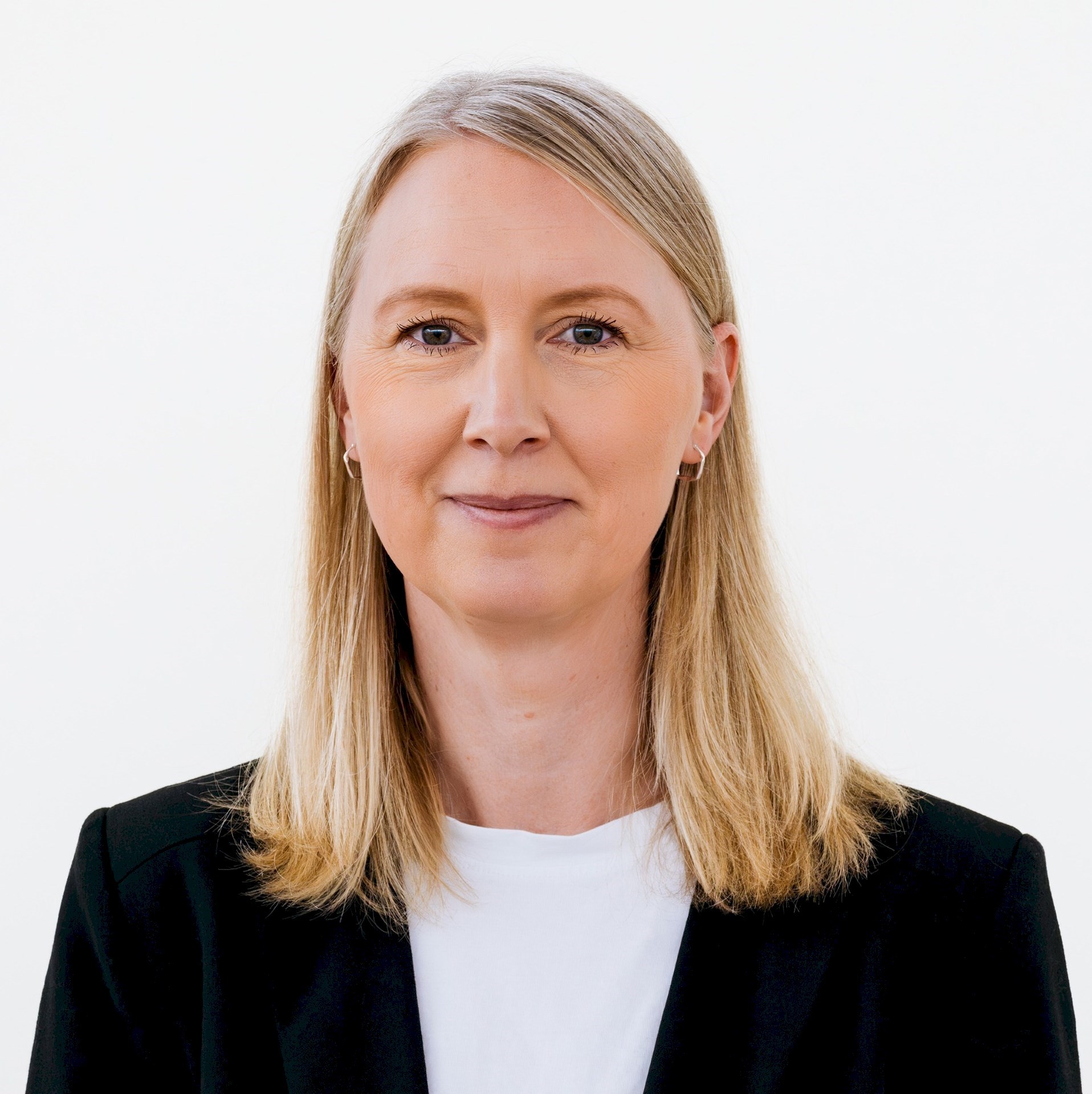 Maria Semberg Person with blond hair wearing a black blazer and white shirt on a white background.