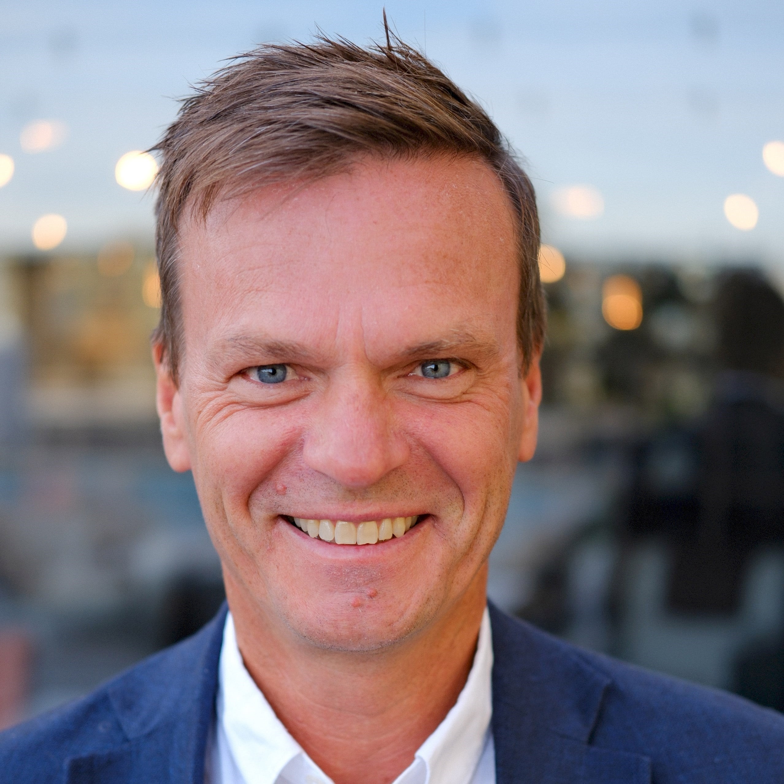 Person i blå kavaj och vit skjorta med en suddig utomhusbakgrund.