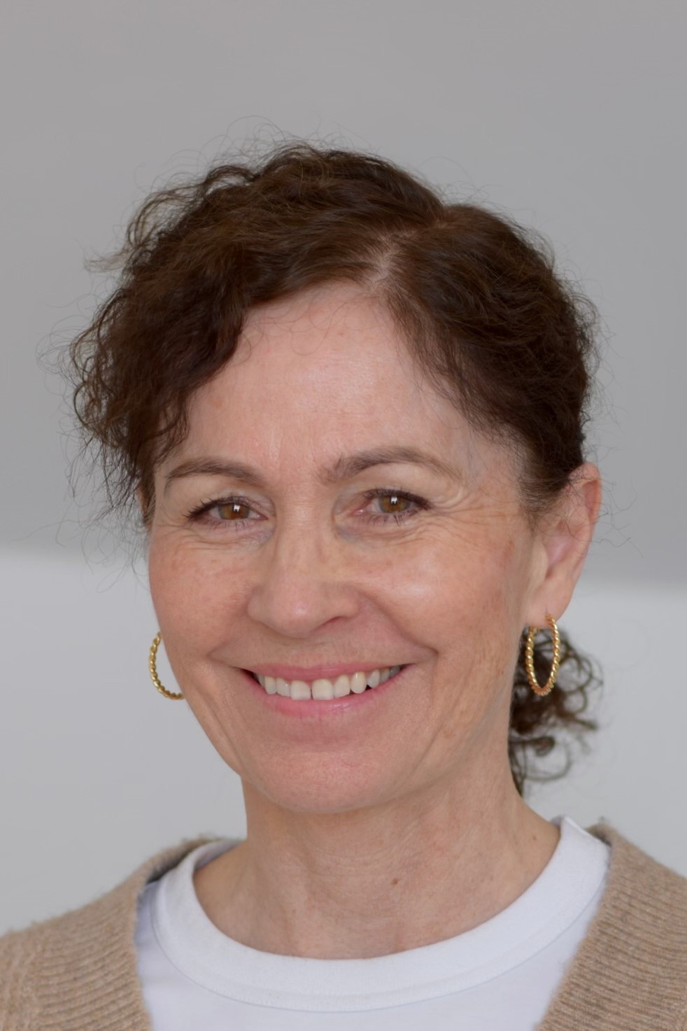 Monica Westerberg Kvinna med lockigt hår som bär en beige sjal och ett långt hängsmycke mot en grå bakgrund.