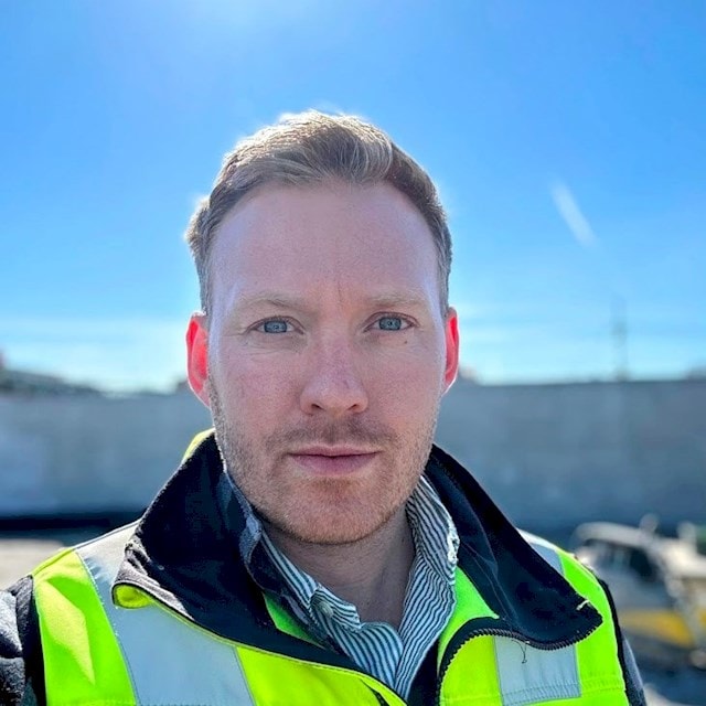 Oscar Paulsson Man in a high-visibility vest outdoors, blue sky in the background, construction site environment.