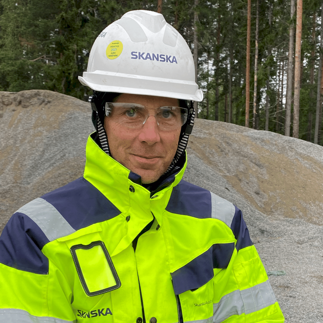 Peter Lundmark En byggnadsarbetare i högsynlighetskläder och en hjälm med Skanska-märke på en grusplats.
