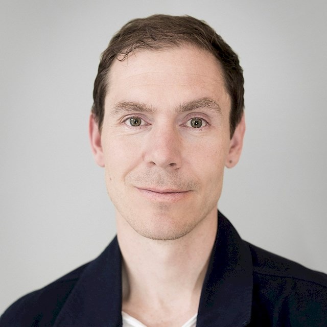 Tim Norrman Schnoor Portrait of a young person with short brown hair wearing a dark jacket and white shirt.