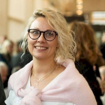 Blond person som bär en rosa tröja över axlarna på ett socialt evenemang.