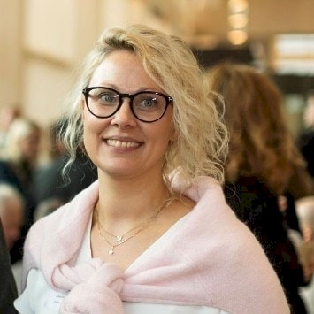 Ulrika Åhs Sivertsen Blond person som bär en rosa tröja över axlarna på ett socialt evenemang.