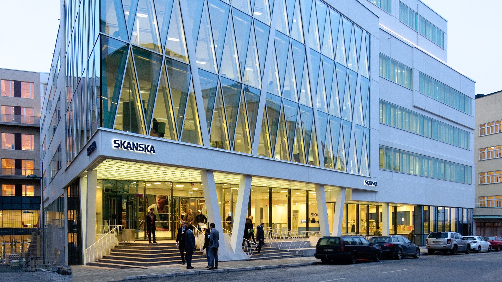 Modern office building with glass facade and people entering Skanska's headquarters.