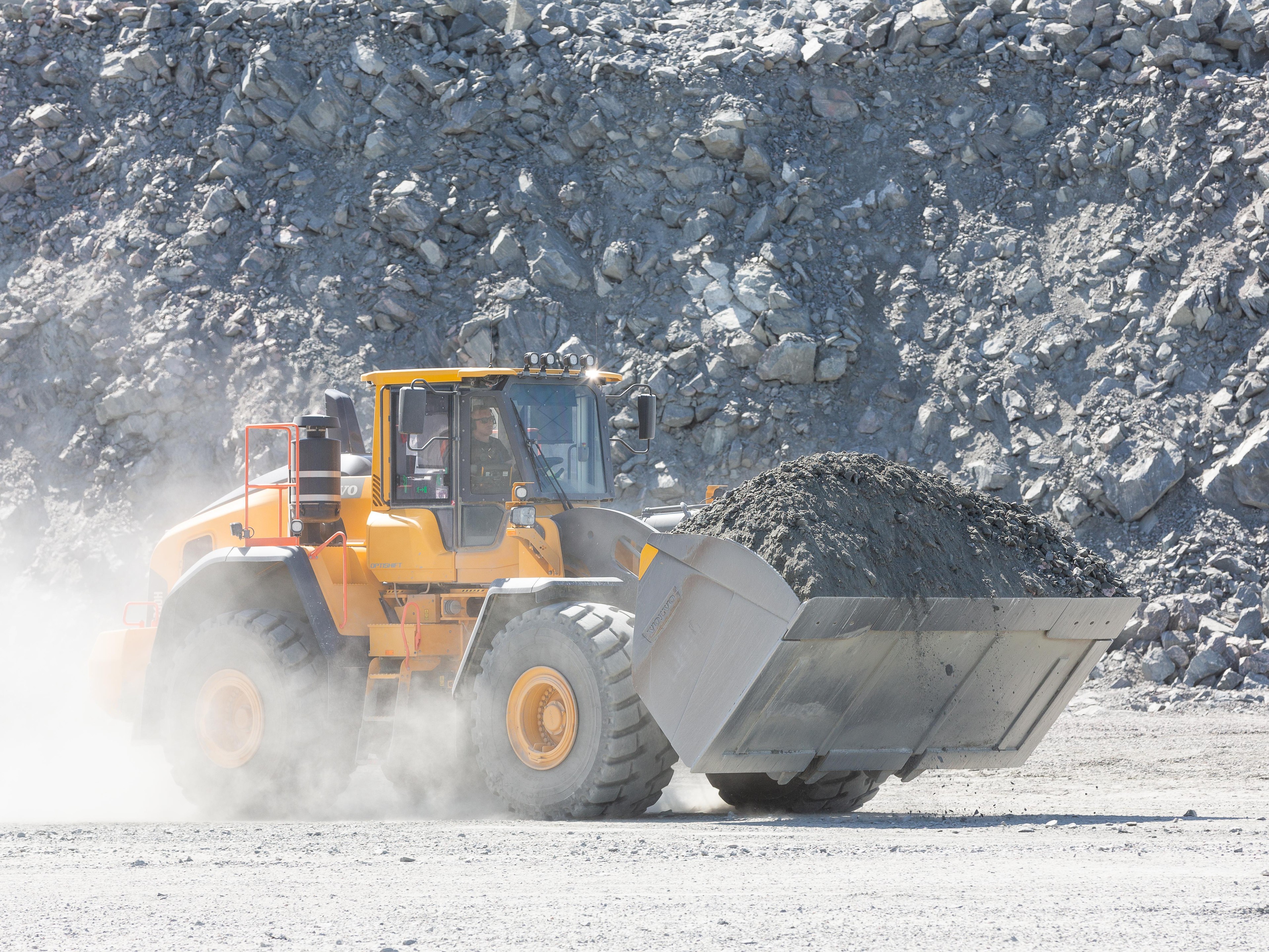 Yellow bulldozer moves a large load of soil in a quarry, surrounded by dust.