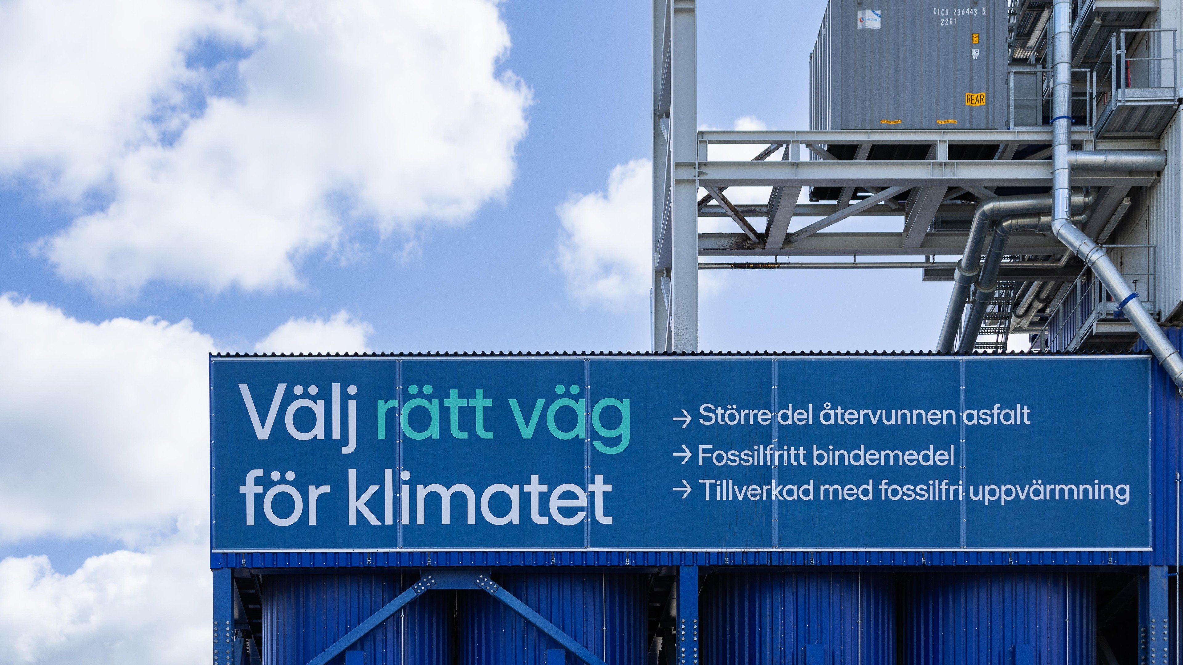 Blå industriskylt med svensk text som främjar klimatvänlig asfaltproduktion.