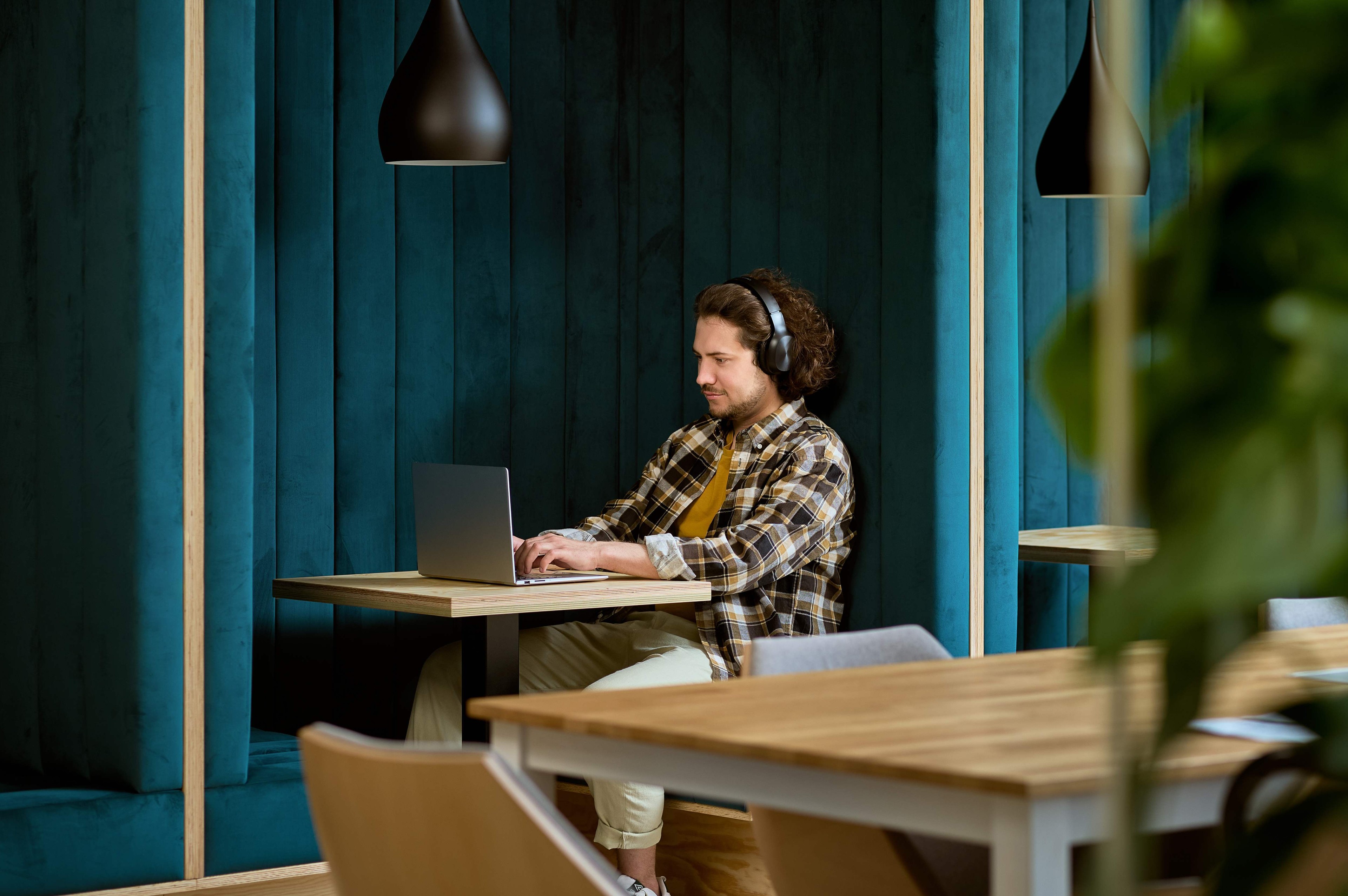 Person som arbetar på en bärbar dator i ett modernt café med teal-färgade väggar och hängande pendellampor.